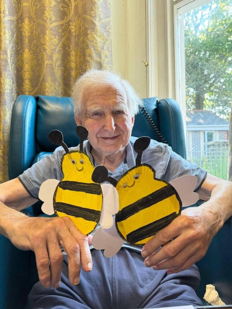 resident holding two painted bees in his hands smiling